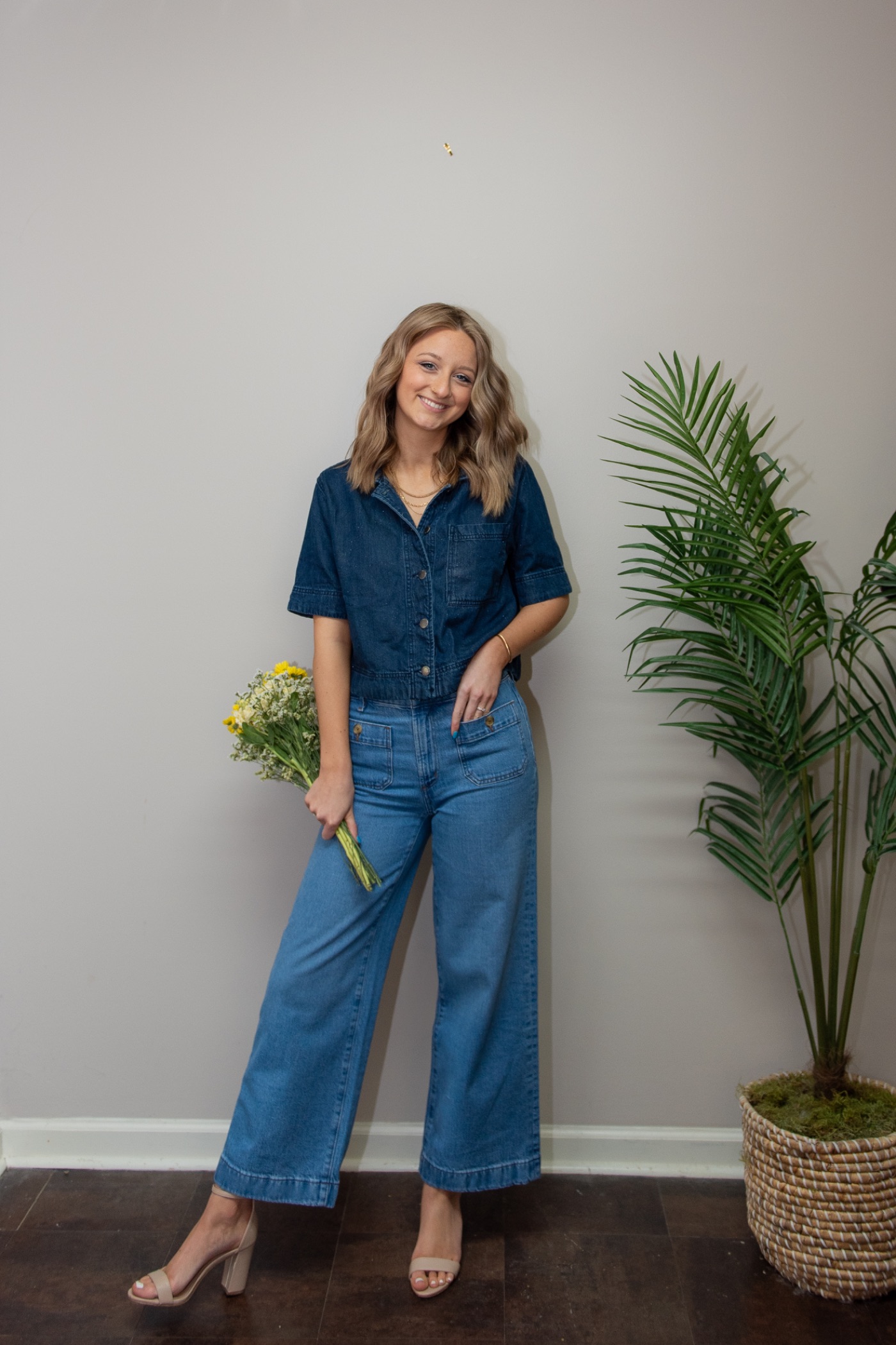 Brooklyn in a denim jumpsuit holding a bunch of flowers.